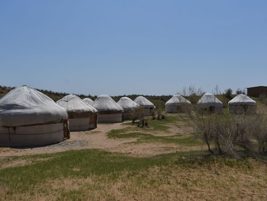 Eine Gruppe von Jurten steht in einer trockenen, sandigen Landschaft unter einem klaren blauen Himmel.