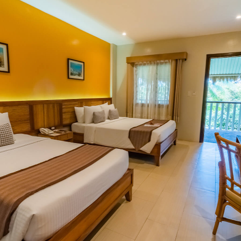 Ein helles Zimmer mit zwei Betten, warmen Farben und einem Balkon, der auf eine grüne Landschaft blickt.