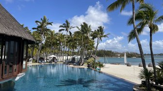 Ein glitzernder Pool umgeben von Palmen, mit einem Blick auf den Strand und das klare Wasser im Hintergrund.