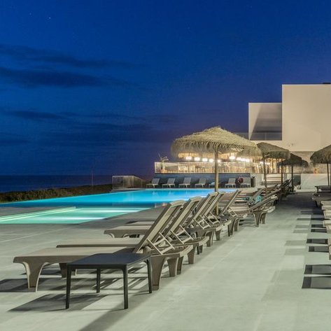 Ein eleganter Poolbereich mit Liegen und Sonnenschirmen, beleuchtet von sanften Lichtern in der Dämmerung am Meer.