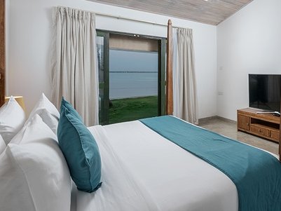 Ein modernes Schlafzimmer mit einem großen Bett, das mit weißen und blauen Kissen dekoriert ist, bietet einen Blick auf einen ruhigen See.