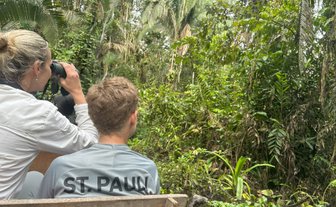 Eine Frau beobachtet mit einem Fernglas die üppige Vegetation des Dschungels, während ein Junge aufmerksam zuschaut.