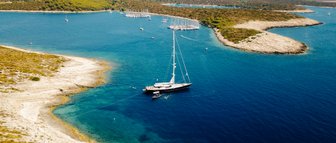 Eine elegante Segelyacht ankert in klarem, blauem Wasser, umgeben von grünen Hügeln und kleinen Buchten.