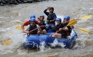Sechs Jugendliche in einem blauen Raftingboot paddeln fröhlich durch einen reißenden Fluss in Costa Rica.