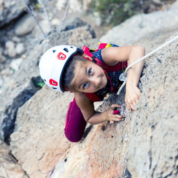 Ein junges Mädchen klettert an einer Felswand, konzentriert und mit einem Helm, während sie sich an einem Seil festhält.
