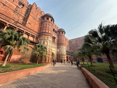 Das Rote Fort in Agra zeigt beeindruckende rote Sandsteinarchitektur, umgeben von üppigen Palmen und einem klaren Himmel.