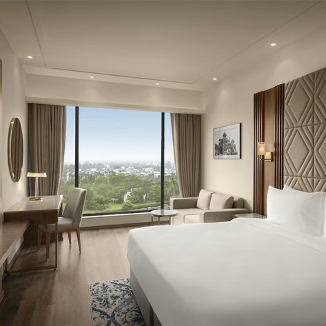 Ein modernes Hotelzimmer mit einem großen Fenster, das einen Blick auf die grüne Landschaft von Delhi bietet.