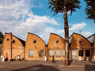 Ein modernes Gebäude mit wellenförmigem Dach, umgeben von Bäumen und einem klaren blauen Himmel, strahlt kreative Atmosphäre aus.