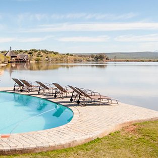 Ein einladender Pool mit Liegen, umgeben von einer ruhigen Landschaft und einem glitzernden See im Hintergrund.