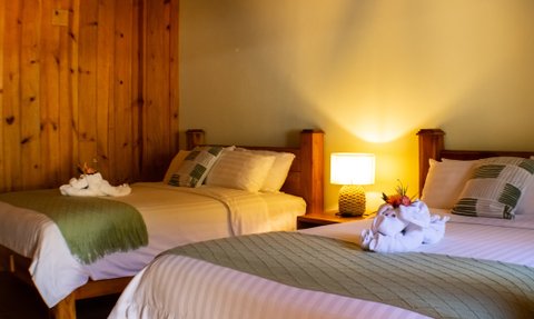 Zwei gemütliche Betten in einem warmen Holzraum, dekoriert mit Handtuch-Tieren und einer sanften Lampe.