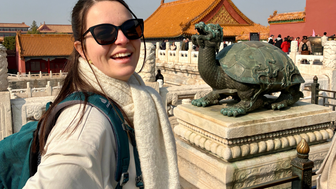 Eine junge Frau mit Sonnenbrille lächelt vor einer Statue einer Schildkröte in der Verbotenen Stadt in Peking.