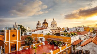 Die Aussicht auf Cartagena zeigt bunte Gebäude und historische Kirchen, während die Sonne am Horizont untergeht.