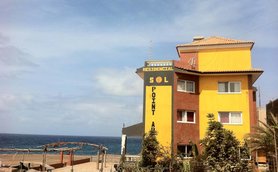 Ein farbenfrohes Gebäude mit der Aufschrift 'Residencial Sol Point' steht am Strand, umgeben von Pflanzen und Meer.