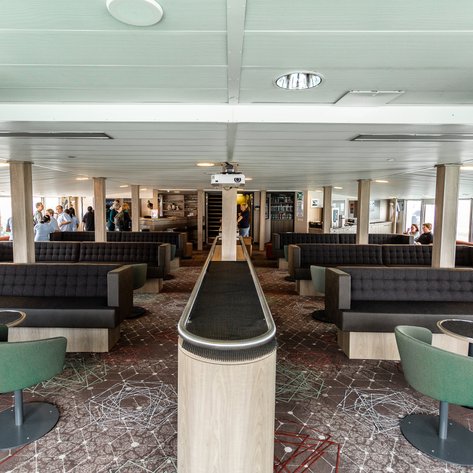 Ein moderner Beobachtungsraum auf einem Schiff, mit bequemen Sitzgelegenheiten und großen Fenstern, die den Blick nach draußen ermöglichen.