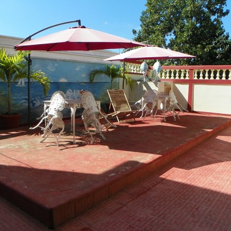 Eine sonnige Dachterrasse mit weißen Möbeln, Sonnenschirmen und einer Wandmalerei mit maritimen Motiven im Hintergrund.