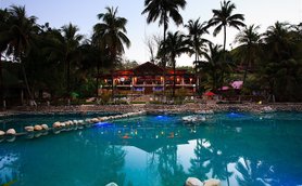 Ein malerisches Resort mit einem klaren Pool, umgeben von Palmen und einer einladenden Holzstruktur im Hintergrund.