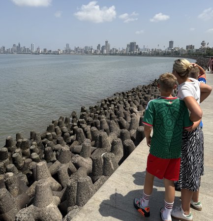 Ein Junge und eine Frau stehen am Ufer, blicken auf die Skyline von Mumbai und genießen den sonnigen Tag am Wasser.