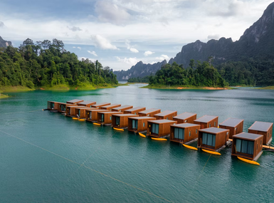 Eine Reihe von modernen, schwimmenden Bungalows liegt auf einem ruhigen, türkisfarbenen See, umgeben von üppiger Natur.