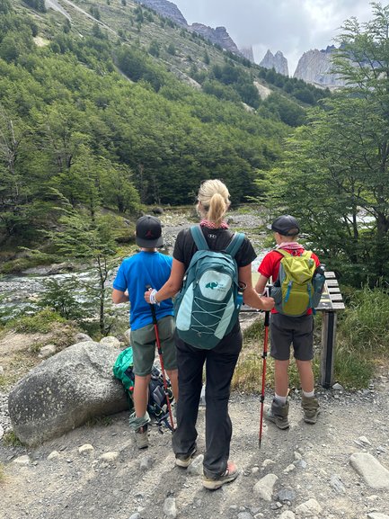 Eine Frau steht mit zwei Kindern am Wanderweg und blickt auf die beeindruckenden Berge im Hintergrund.
