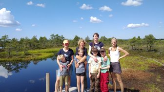 Eine fröhliche Familie steht auf einem Steg, umgeben von einer malerischen Landschaft mit Wasser und Bäumen.