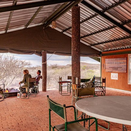 Eine Gruppe von vier Personen sitzt entspannt in einem überdachten Bereich und genießt die Aussicht auf die Natur.