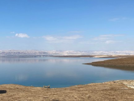 Der ruhige Wasserspiegel des Toten Meeres spiegelt die sanften Hügel und den klaren blauen Himmel wider.