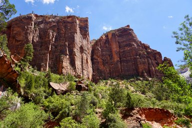 Majestätische Felsen erheben sich über üppige grüne Vegetation im Zion-Nationalpark unter einem strahlend blauen Himmel.