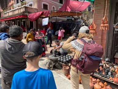 Eine Gruppe von Menschen beobachtet einen Töpfer, der kunstvolle Töpfe in einer belebten Straße in Bhaktapur formt.