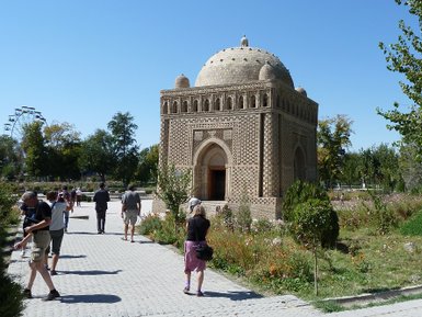 Eine Gruppe von Touristen erkundet das Samaniden-Mausoleum, umgeben von üppigem Grün und bunten Blumen im Park.