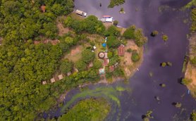 Ein Blick aus der Vogelperspektive auf das grüne Amazonasgebiet mit einem kleinen Lodge-Resort in der Mitte.
