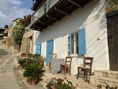 Ein traditionelles zypriotisches Haus mit blauen Fensterläden und einem einladenden Eingangsbereich, umgeben von Pflanzen.