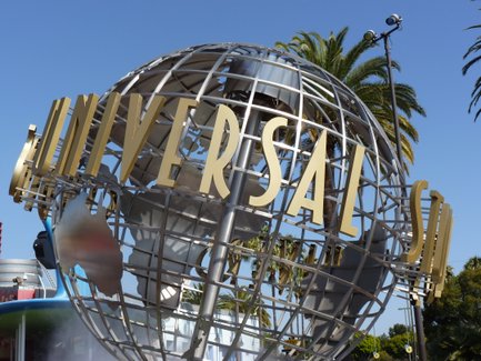 Die goldene Schrift 'UNIVERSAL' thront über einer stilisierten Weltkugel, umgeben von Palmen und klarem blauen Himmel.