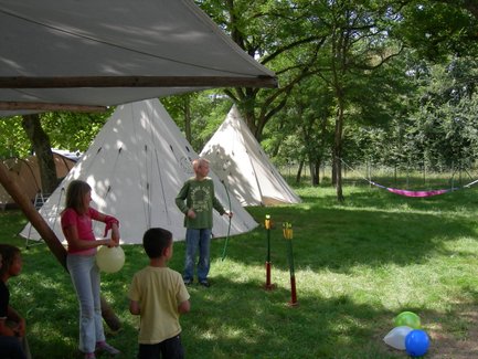 Eine Gruppe von Kindern spielt im Freien, umgeben von Zelten und Bäumen, während sie mit Luftballons und Pfeilen interagieren.