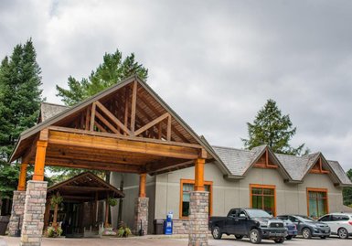 Die Außenansicht eines Resorts mit einem großen Holzvordach und modernen Fenstern, umgeben von Bäumen und Autos.