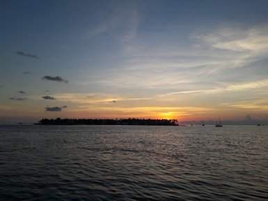 Ein atemberaubender Sonnenuntergang über dem Wasser, mit sanften Wellen und einer silhouettierten Insel im Hintergrund.