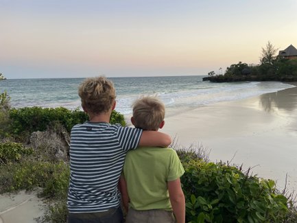 Zwei Jungen stehen am Strand, umarmt, während sie den Sonnenuntergang über dem Meer beobachten.