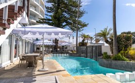 Ein einladender Poolbereich mit Sonnenschirmen und Liegen, umgeben von Palmen und blühenden Pflanzen, strahlt Entspannung aus.