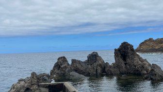Eine ruhige Küstenlandschaft mit schroffen Felsen, die aus dem klaren Wasser ragen, unter einem bewölkten Himmel.