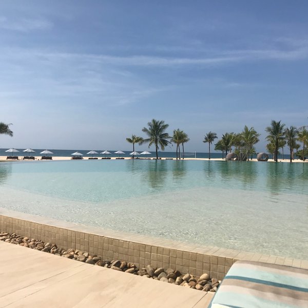 Ein ruhiger Pool mit klarem Wasser, umgeben von Palmen und Liegen, bietet einen atemberaubenden Blick auf das Meer.
