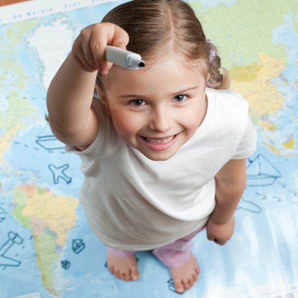 Ein fröhliches Mädchen steht auf einer Weltkarte und hält einen Marker, bereit, etwas zu zeichnen oder zu markieren.