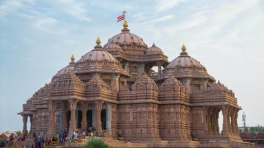 Der Akshardham-Tempel erhebt sich majestätisch mit kunstvollen Verzierungen und beeindruckenden Kuppeln unter einem blauen Himmel.