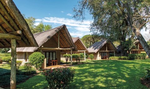 Eine idyllische Gartenlandschaft mit mehreren Chalets, umgeben von üppigem Grün und strahlend blauem Himmel.