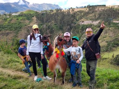 Eine Gruppe von Menschen posiert fröhlich mit zwei Lamas in einer malerischen Berglandschaft.