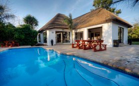 Ein einladendes Gästehaus mit Strohdach, umgeben von üppigem Grün und einem glitzernden Pool im Vordergrund.