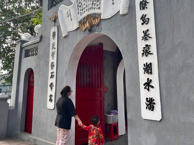 Eine Frau und ein Kind stehen vor einem grauen Gebäude mit roten Türen und chinesischen Schriftzeichen an der Wand.