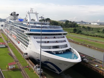Ein großes Kreuzfahrtschiff passiert die Miraflores-Schleuse im Panamakanal, umgeben von grüner Landschaft und Zuschauern.