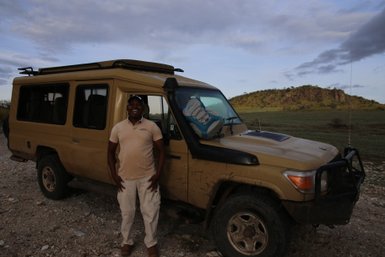 Safari-Guide lächelt am Safarijeep bei Abendstimmung – Tansania Familienreise
