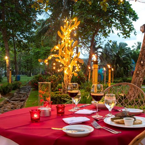 Ein romantisch gedeckter Tisch im Freien, umgeben von üppigem Grün und sanftem Licht, ideal für ein Abendessen bei Sonnenuntergang.