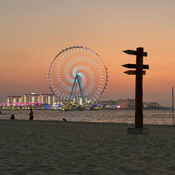 Ein Riesenrad leuchtet in bunten Farben vor einem malerischen Sonnenuntergang über dem Wasser.