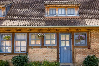 Die Fassade eines charmanten Hauses mit blauen Fenstern und einer blauen Tür, umgeben von bunten Blumen und Pflanzen.